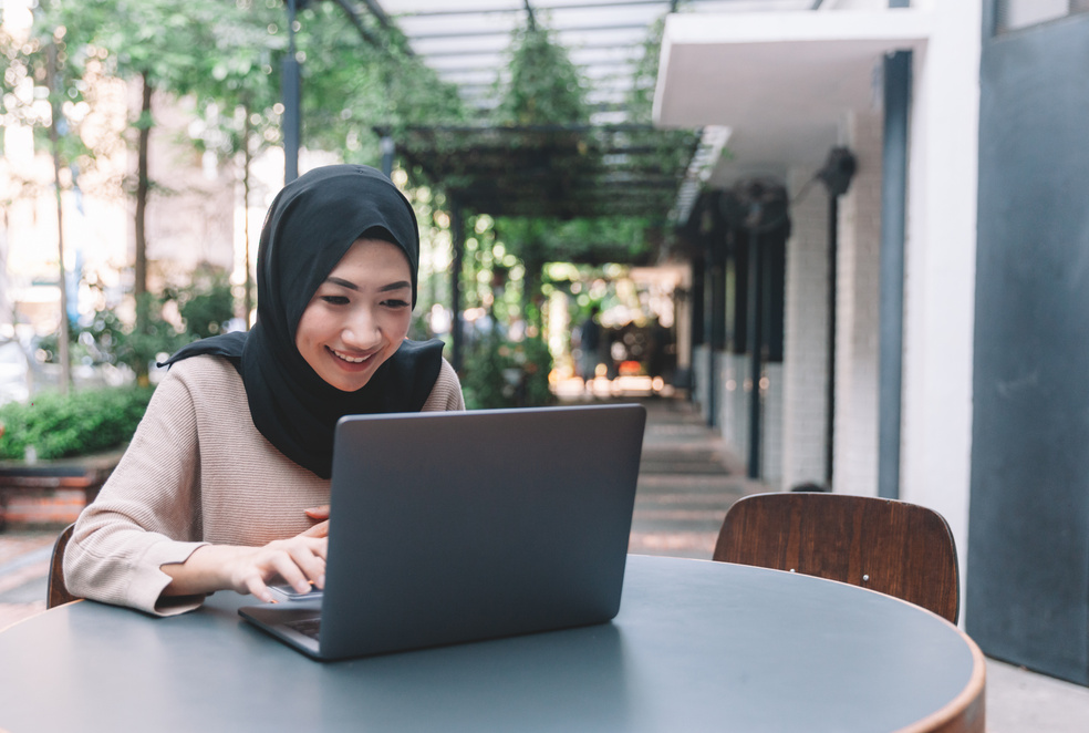 Asian Malaysian Malay working using laptop at cafe smiling